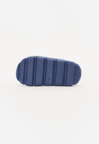 Suola di scarpa in gomma blu con texture rigata, dotata di punta e tallone arrotondati. Solchi evidenti per aderenza e piccolo dettaglio di branding circolare.