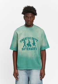 Grøn gradient oversized t-shirt med rund halsudskæring og korte ærmer. Indeholder teksten "CREATIVE DEPT" og "RETERNITY" med grafiske figurer.