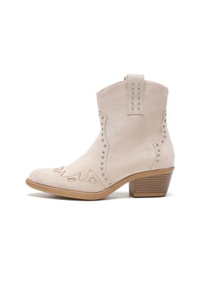 Botín de ante beige con costuras decorativas y acentos de tachuelas plateadas, que presenta un tacón bloque y un diseño de punta afilada.