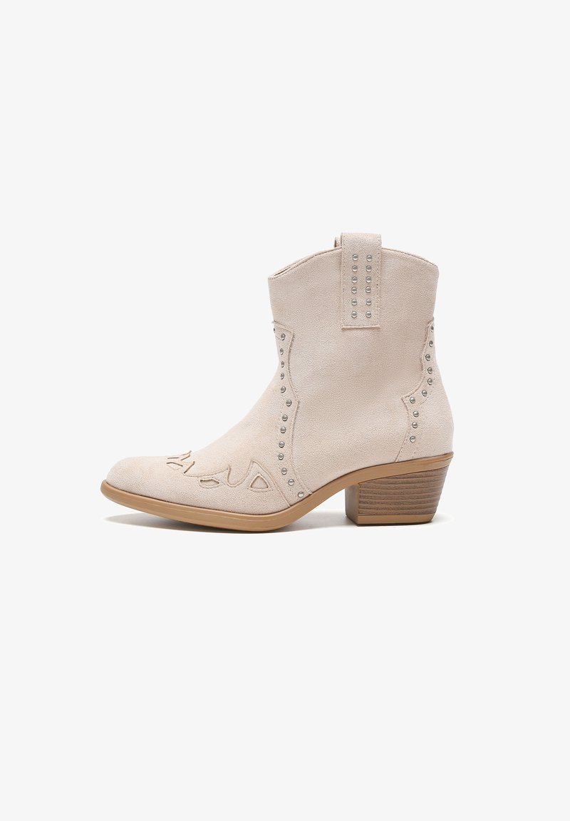 Botín de ante beige con costuras decorativas y acentos de tachuelas plateadas, que presenta un tacón bloque y un diseño de punta afilada.