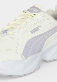 Λευκό και ανοιχτό μωβ sneaker Puma με κορδόνια και χοντρή λευκή σόλα, που δείχνει το πλευρικό λογότυπο και λεπτομέρειες του σχεδίου.