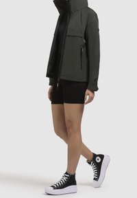 Mörkgrön lättviktsjacka med hög krage, dragkedja framtill och två sidofickor, ihopparad med en åtsittande svart bodysuit och svarta platåskor.