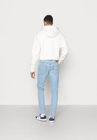 Vit kortärmad hoodie med huva, kombinerad med ljusblå slim-fit jeans och marinblå sneakers, vilket visar en ren och minimal design.