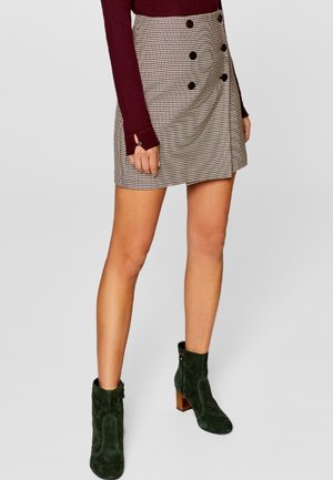 Minirok in pied-de-poule met een hoge taille, met dubbele knopen. Het model draagt groene suède enkellaarsjes met een grove hak.