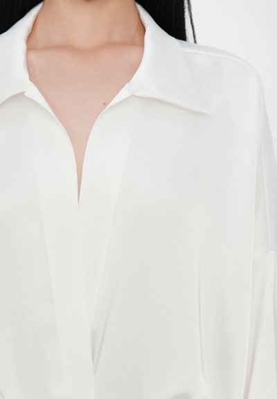 White silk blouse with a collar and a deep V-neckline, featuring smooth texture and soft draping on the sides.