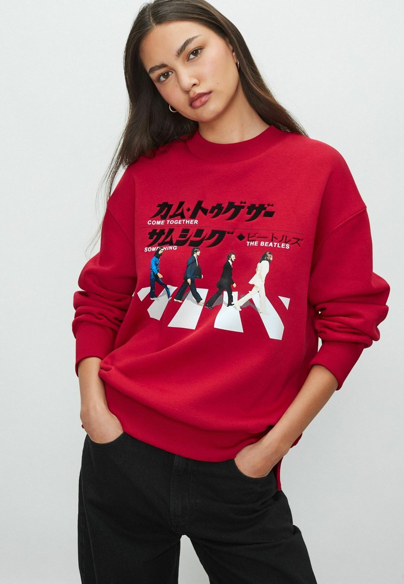 Punane sweatshirt, millel on graafiline trükk, mis on inspireeritud The Beatles'ist, valge teksti ja tänava ületamise disainiga. Kootud mansetid ja äär.