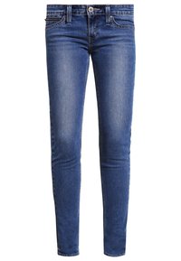 Jeans ajustados en denim azul medio. Presentan un diseño clásico de 5 bolsillos, cierre de cremallera y costuras en contraste. Textura suave con ligero desvanecimiento.