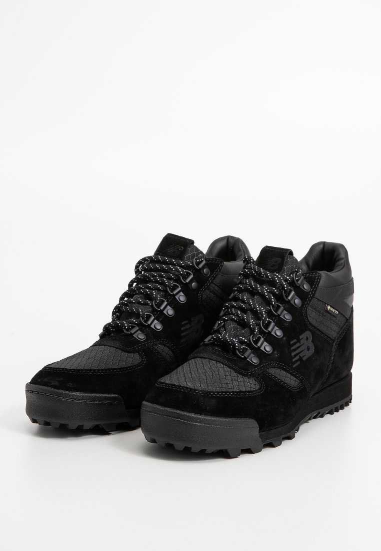 Sneakers neri alti realizzati in suede e mesh, con pannelli testurizzati, dettagli riflettenti e lacci a contrasto. La suola in gomma garantisce trazione.
