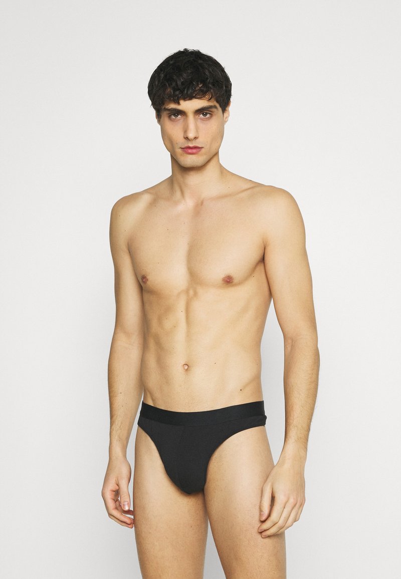 Black men's briefs with a smooth texture, low-rise design, and a wide waistband, displayed on a male model with a neutral background.