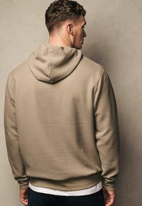 Beige Kapuzenpullover aus strukturiertem Stoff, mit Kapuze und gerippten Bündchen. Die Rückseite verfügt über ein nahtloses Design und einen elastischen Taillenbund.