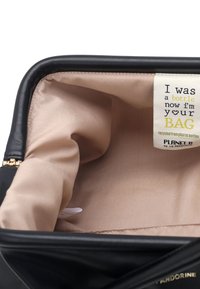 Interno di borsa nera con texture e fodera liscia color beige chiaro. L'etichetta recita: "Ero una bottiglia, ora sono la tua BORSA, riciclata da bottiglie di plastica."