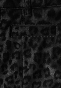 Tessuto in pelliccia sintetica nera con un sottile motivo a leopardo. La texture è morbida e presenta una finitura lucida, arricchita da cuciture a contrasto.