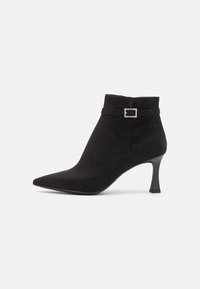 Bottine en suede noire avec un bout pointu, un talon fin et un accent décoratif de boucle sur la bride de cheville. Texture lisse sur toute la chaussure.