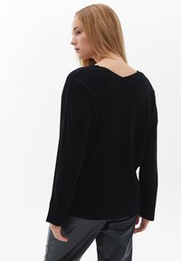 Schwarzer Strickpullover mit tiefem V-Ausschnitt, gerippten Bündchen und Saum. Mit lockerer Silhouette und weicher Textur. Keine auffälligen Muster oder Verzierungen.