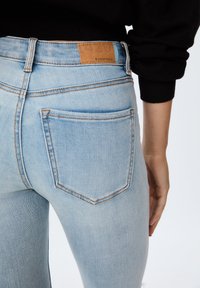 Svetlo modre skinny kavbojke z visokim pasom, ki imajo zadnje žepke in subtilno zbledelost. Oznaka vidna na pasu označuje blagovno znamko.