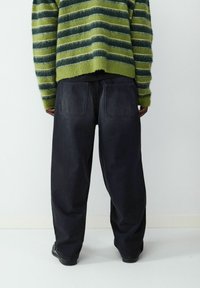 Zielono-granatowy sweter w paski, pokryty miękkim futerkiem, zestawiony z luźnymi, ciemnymi dżinsami z dużymi tylniymi kieszeniami i swobodnym krojem.