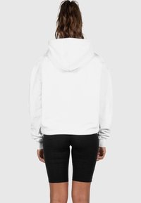 Hvit hettegenser sett fra bak, med en avslappet passform og ribbede mansjetter, kombinert med svarte sykkelshorts.