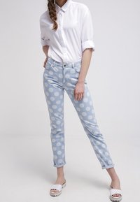 Ljusblå denimjeans med vita prickar, smal passform, framfickor och knappstängning. Kombinationen med en vit skjorta med knappar och sandaler.