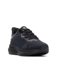 Zapatilla deportiva negra con parte superior de malla texturizada, cuello acolchado y suela de goma. Presenta un cierre con cordones y acentos reflectantes en el lateral.