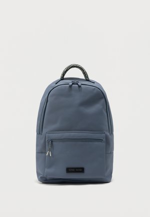 Sac à dos bleu avec poche zippée à l'avant et poignée tressée en haut sur un fond clair uni.