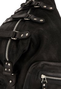 Zwarte leren tas met textuur, zilveren rits en drie gespbanden op een witte achtergrond.