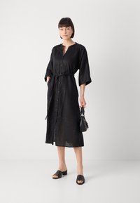 Μαύρο μεσάτο φόρεμα από λινό με ζώνη στη μέση, κουμπιά μπροστά και φαρδιά μανίκια. Συνδυασμένο με μαύρες τακούνες μούλ και μια μικρή μαύρη τσάντα.