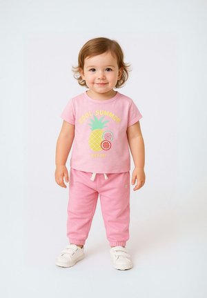 Camiseta de manga corta rosa claro con gráfico de piña y texto "VERANO GENIAL", combinada con pantalones de chándal rosa a juego y zapatillas blancas.