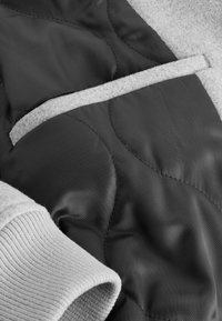 Quilted black fabric with smooth texture, featuring a gray ribbed cuff and a light gray felt accent. Patterns of curved stitching visible.