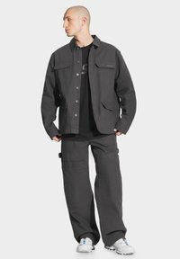 Szara bawełniana kurtka z zapięciem na guziki z przodu i dwoma kieszeniami na piersi, w zestawie z dopasowanymi spodniami cargo z wieloma kieszeniami i szerokim krojem nogawek.