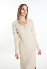 Pulover tricotat de culoare crem, cu decolteu în V și textură ribbed. Prezintă mâneci lungi și o siluetă ajustată cu patternuri geometrice.
