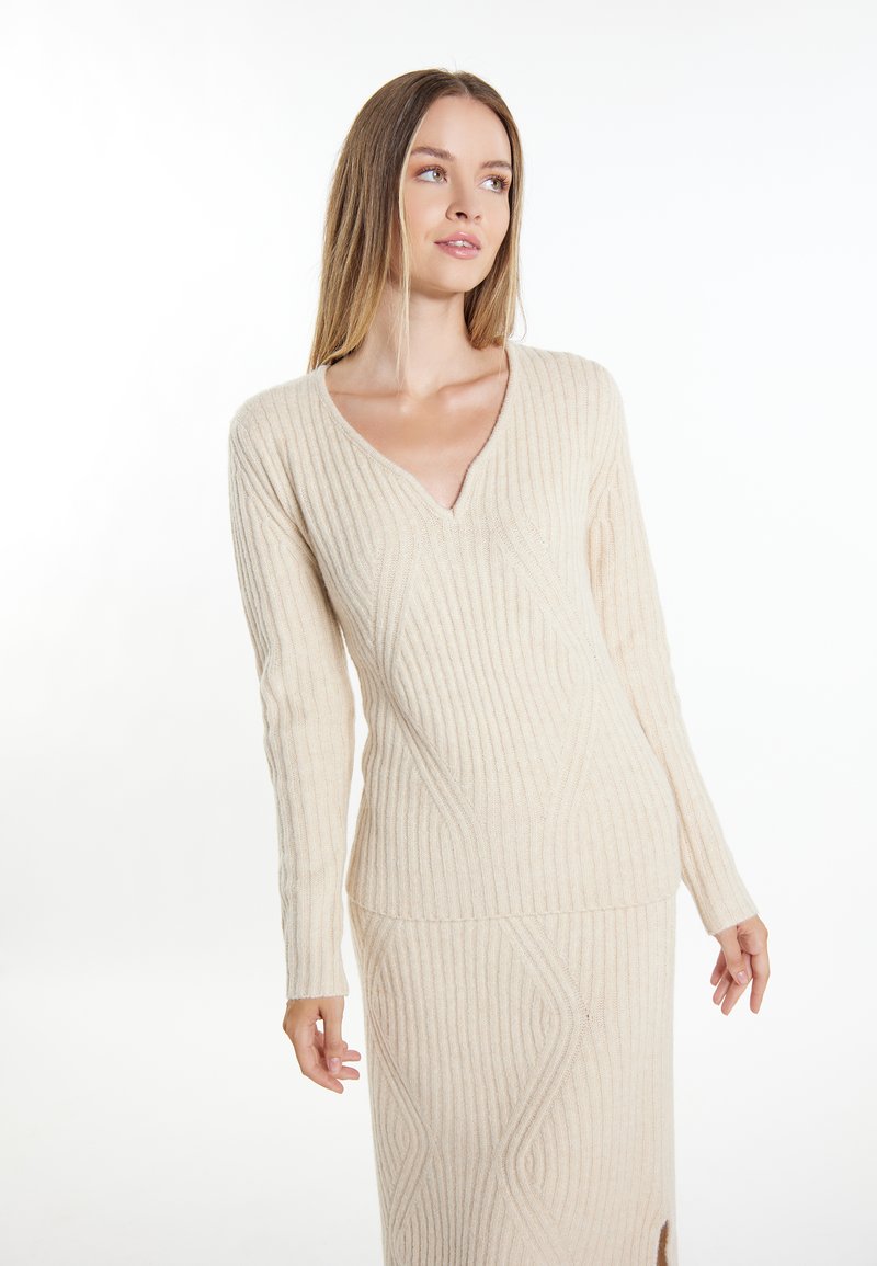 Pulover tricotat de culoare crem, cu decolteu în V și textură ribbed. Prezintă mâneci lungi și o siluetă ajustată cu patternuri geometrice.