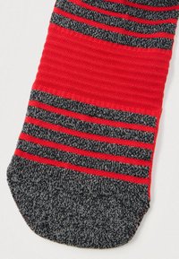 Κόκκινη και σκούρα γκρι πλεκτή κάλτσα με οριζόντιες ρίγες και σόλο σκούρα γκρι περιοχή στα δάχτυλα σε λευκό φόντο.