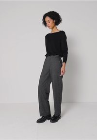 Šedé vlněné kalhoty s volnými nohavicemi a vysokým pasem, s jemnou texturou, v kombinaci s přiléhavým černým topem s dlouhým rukávem a černými botami.