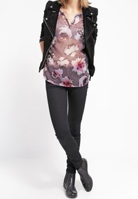 Giacca in suede nera sopra una blusa floreale e trasparente con fiori rosa e bianchi. Jeans neri aderenti e stivaletti completano l'outfit.