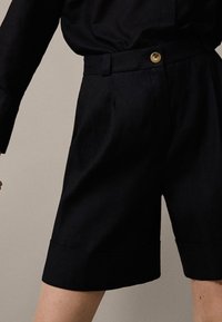 Mörkblå skräddarsydda shorts i lätt tyg med sidfickor, knappstängning och uppvikta fållar.