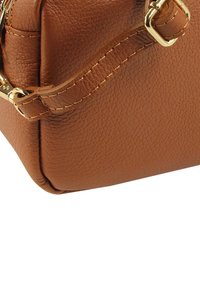 Hellbraune Lederhandtasche mit strukturierter Oberfläche, goldfarbenen Beschlägen und detaillierter Naht entlang der Nähte und des Riemens.