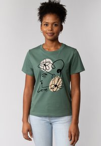 T-shirt en coton vert avec un design de visage et de fleurs en art linéaire minimaliste, accompagné du texte "Love" en script noir. Manches courtes.