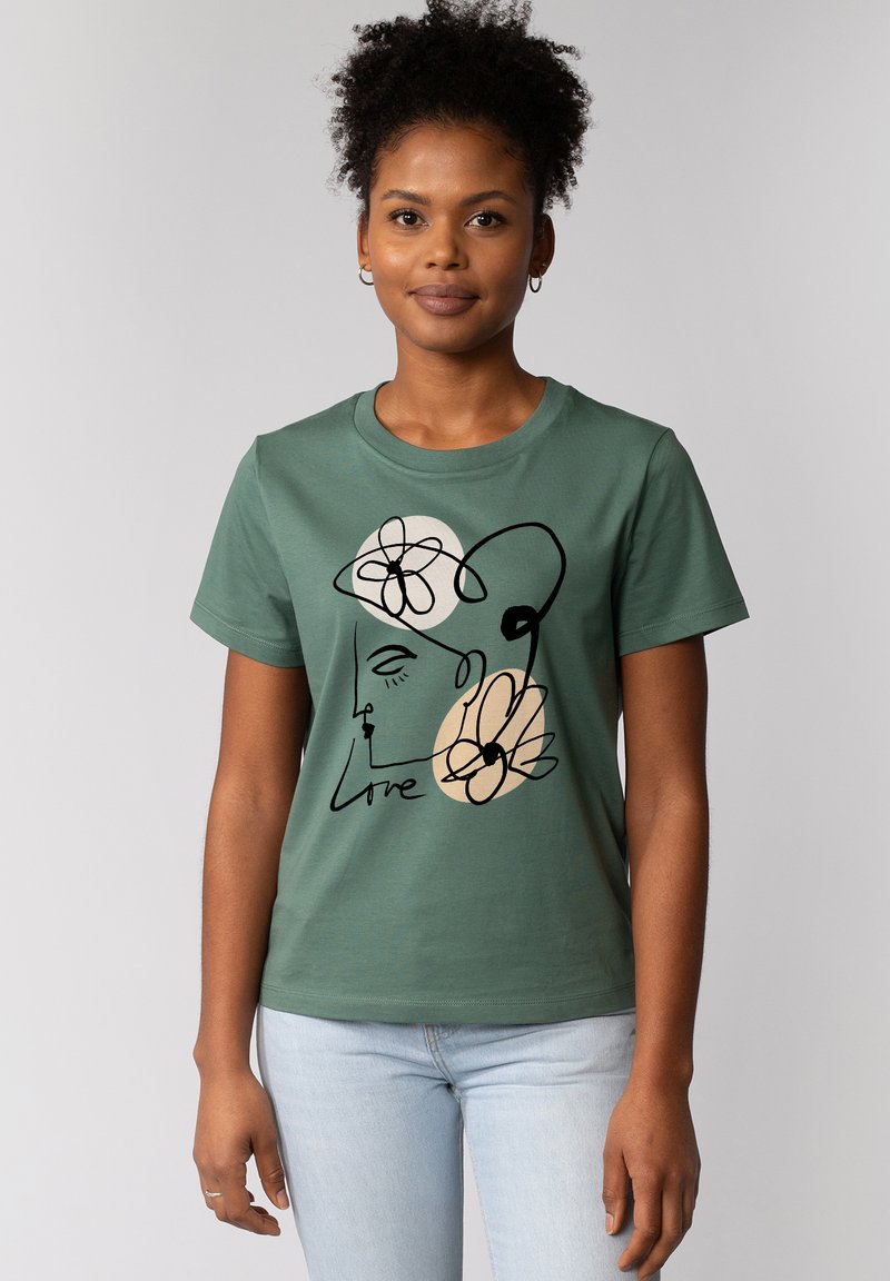 T-shirt en coton vert avec un design de visage et de fleurs en art linéaire minimaliste, accompagné du texte "Love" en script noir. Manches courtes.