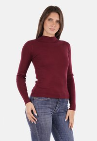 Maglione a maniche lunghe bordeaux a coste con colletto alto, design aderente e texture morbida, abbinato a jeans in denim blu.