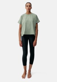 Gaiši zaļš kaste veida T-krekls ar īsām piedurknēm un apaļu kakla izgriezumu, savienots ar melniem pieguļošiem legingiem ar sānu šuvēm un kabatām.