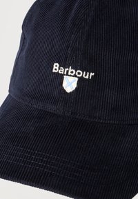 Σκούρο μπλε ναυτικό καπέλο μπέιζμπολ από κορδούρο με κεντημένο λογότυπο Barbour και ασπίδα σε λευκό και ανοιχτό μπλε στην μπροστινή επιφάνεια.