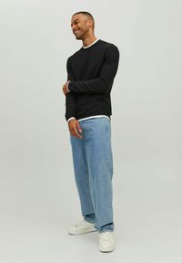 Felpa nera con collo bianco, abbinata a jeans a gamba dritta blu chiaro e sneakers bianche. Il modello si trova in una postura rilassata.