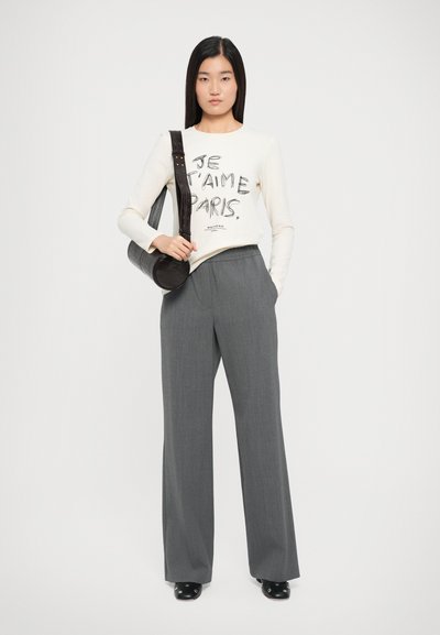 Long-sleeve cream t-shirt with "JE T'AIME PARIS" print in black, paired with loose, gray, high-waisted trousers and a circular black bag.