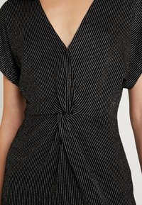 Svart klänning med silver vertikala ränder. Har en V-ringning och korta ärmar, knuten i midjan med en detalj. Mjuk textur.