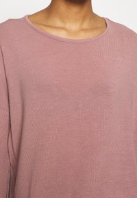 Maglione rosa chiaro con scollo rotondo e maniche lunghe. Il tessuto è morbido, con una trama a coste e una vestibilità rilassata.