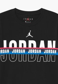 Black cotton T-shirt featuring bold white "JORDAN" text with a red and blue striped band. Includes a white Jumpman logo above the text.