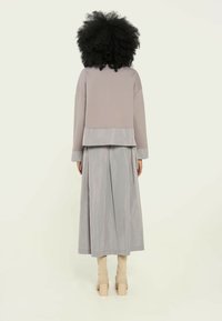 Top en gris claro con capas y un diseño corto, combinado con una falda larga plisada. Presenta texturas suaves y tonos neutros. Tacones beiges apilados.