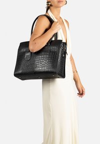 Borsa a tracolla in pelle nera con texture coccodrillo, hardware in acciaio inox, doppio manico, dotata di un'etichetta removibile e quattro piedi metallici alla base.