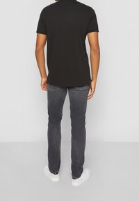 T-shirt noir en coton à manches courtes, porté avec un jean gris foncé et des baskets blanches, vu de dos. Pas de motifs ou d'accents notables.