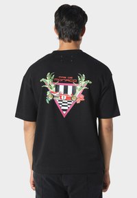 Mustat puuvillaiset T-paidat, joissa on värikäs graafinen kuvitus: palmulehtiä, punainen kilpa-auto ja ruutukuviota vaaleanpunaisessa kolmiossa.